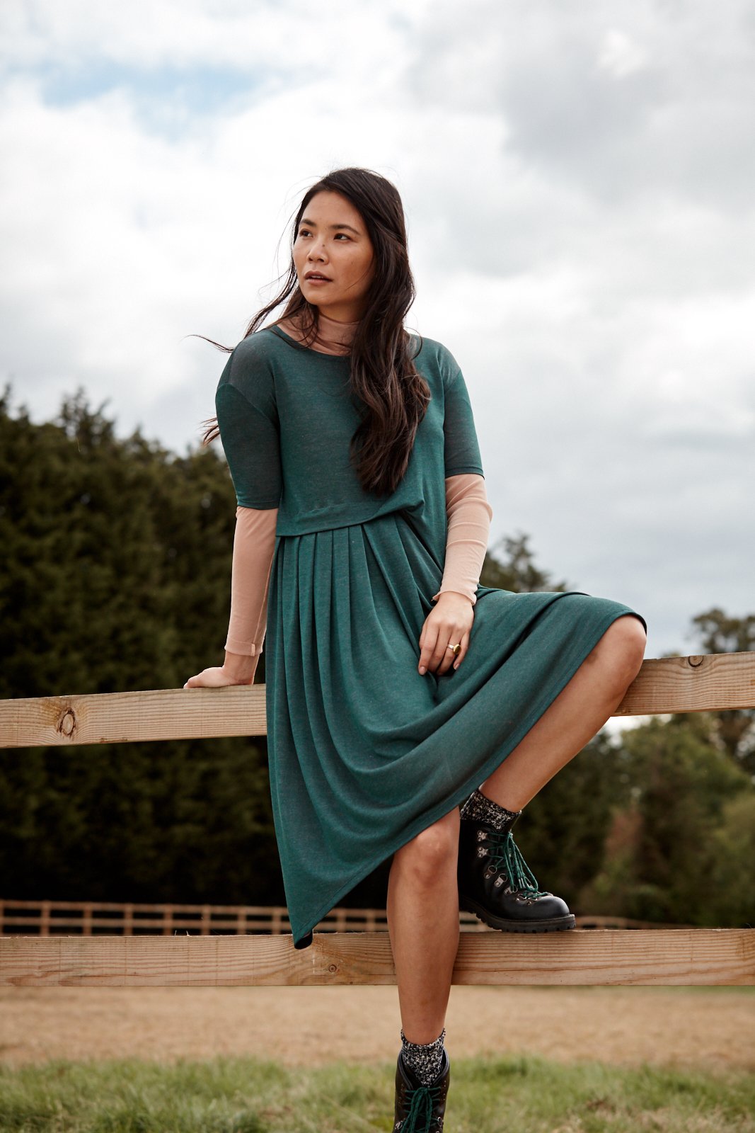 Woman wearing the Asmuss Asymmetric Pleat Dress in Pine Green.  A stylish, sustainable addition to the moderns woman's wardrobe