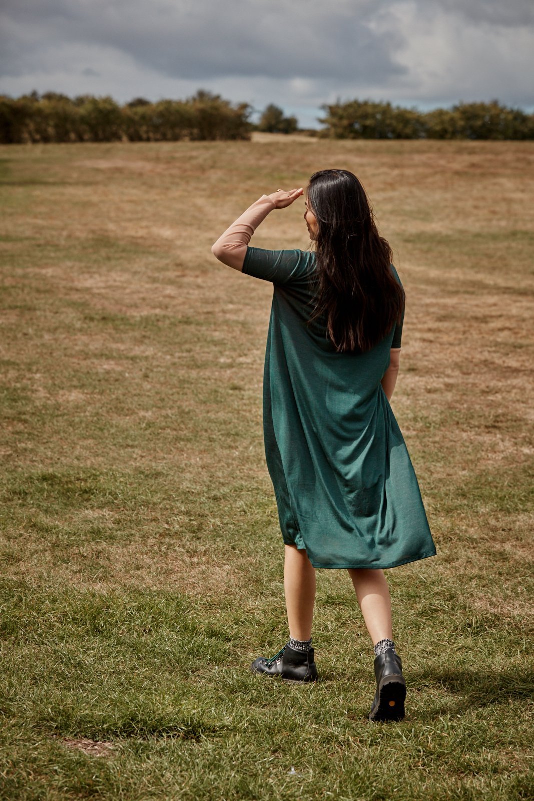 Woman wearing the Asmuss Asymmetric Pleat Dress in Pine Green.  Wear it in the office, outdoors or where ever you travel to