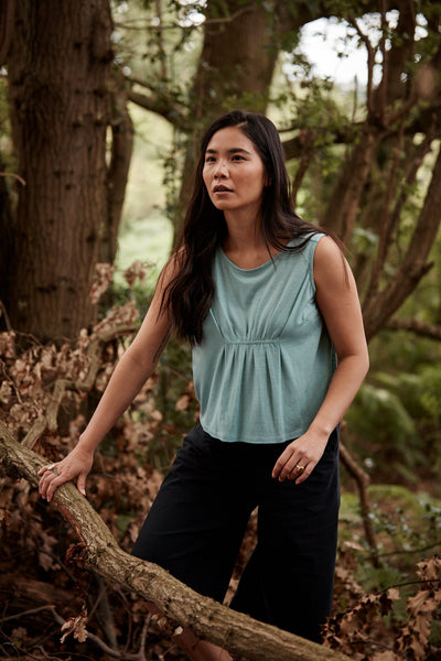Woman exploring the woods in a Asmuss Pleated Tank in Sea Green.  Stylish, sustainable performance womenswear for any adventure.