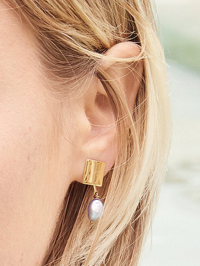 Close up of model's ear with gold square stud blue pearl earring