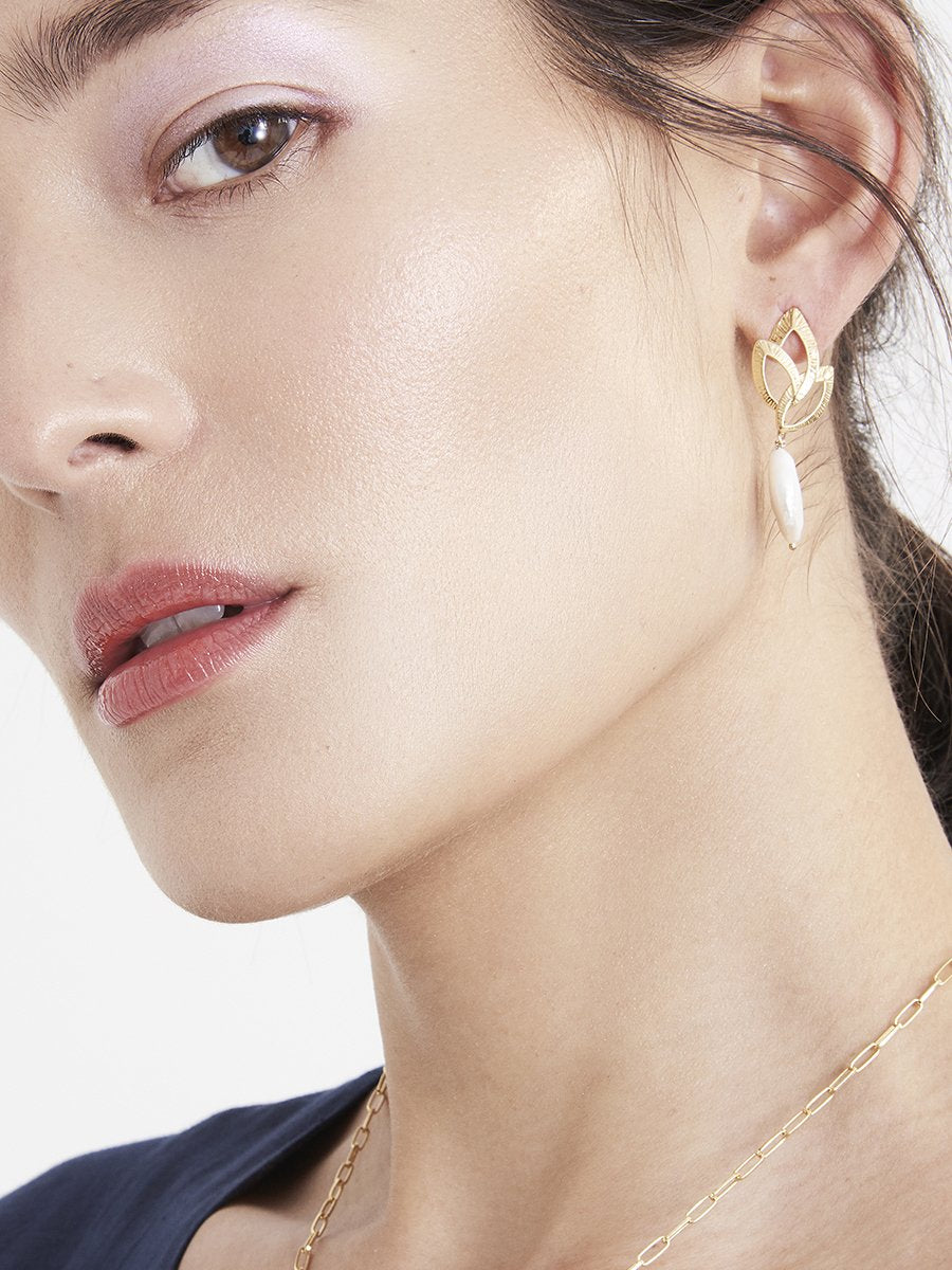 Model wearing gold leaf earrings with pearls in blue top