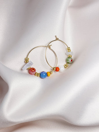 Gold hoops with colourful beads on a fabric background