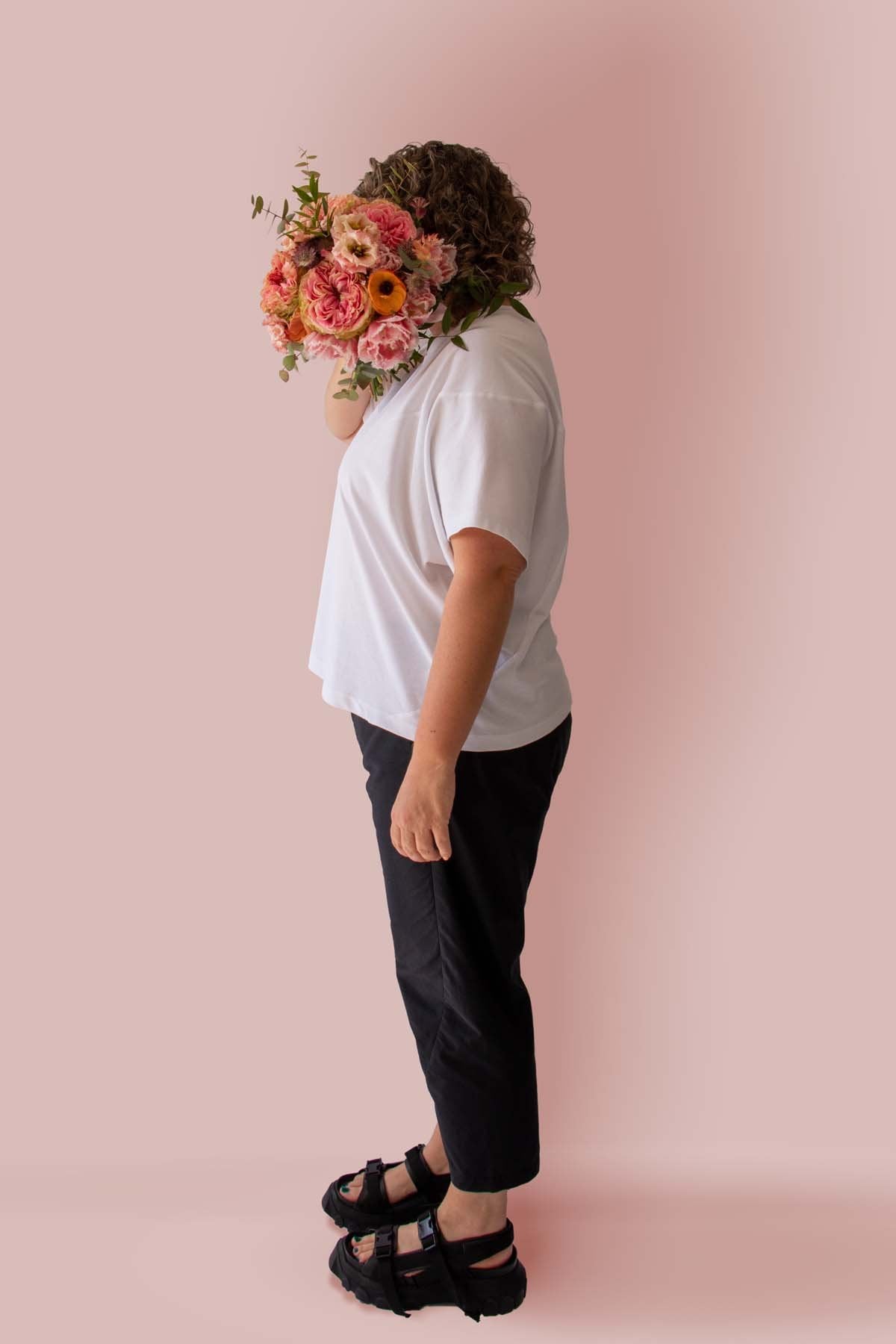 Side view of Asmuss Panelled T-shirt in White Organic Cotton and Recycled Polyester worn by Clare with a beautiful bunch of flowers in front of her face.