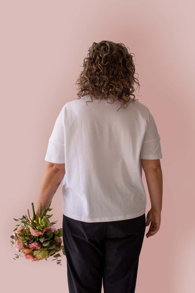 Back view of Asmuss Boxy T-shirt in White Organic Cotton and Recycled Polyester with Embroidered Rose detail worn by Clare holding a beautiful bunch of flowers, that echo the embroidery.